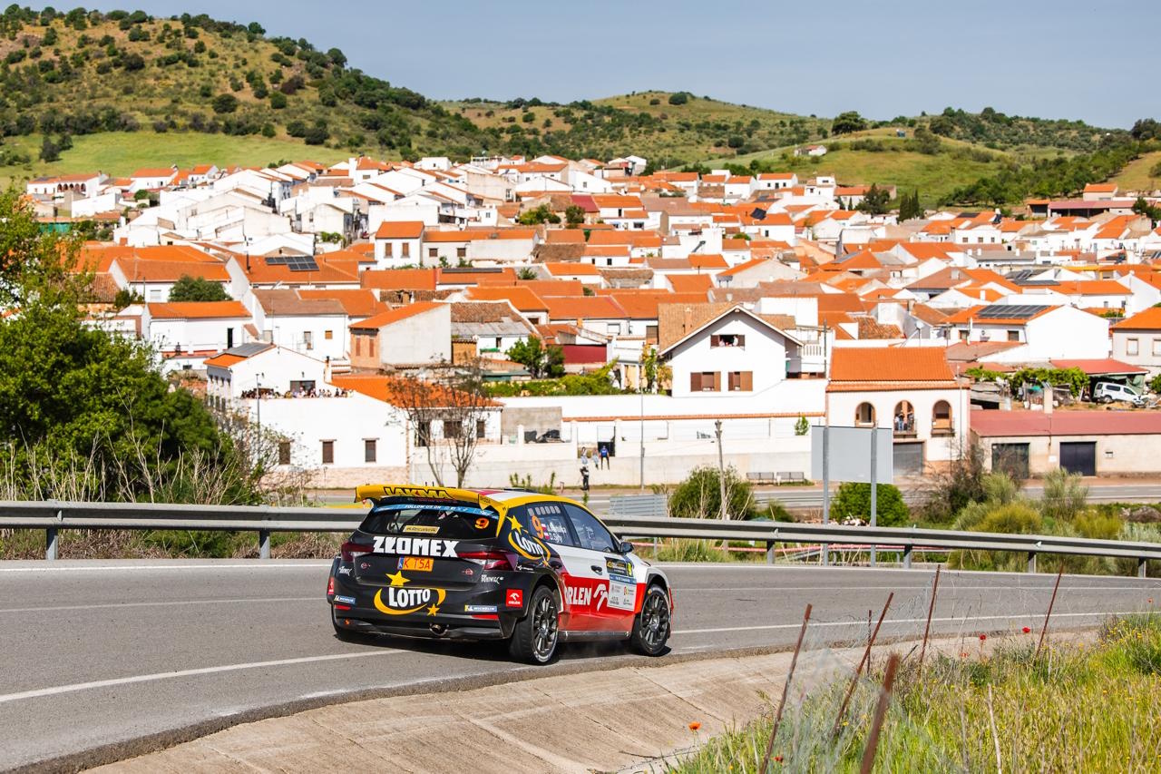 Samochód rajdowy Polaków jadący na tle białych domków z czerwonymi dachami