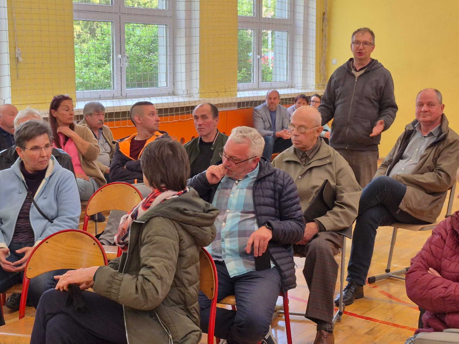 ludzie siedzący na krzesłach i zadający pytania podczas spotkania konsultacyjnego w Ostropie