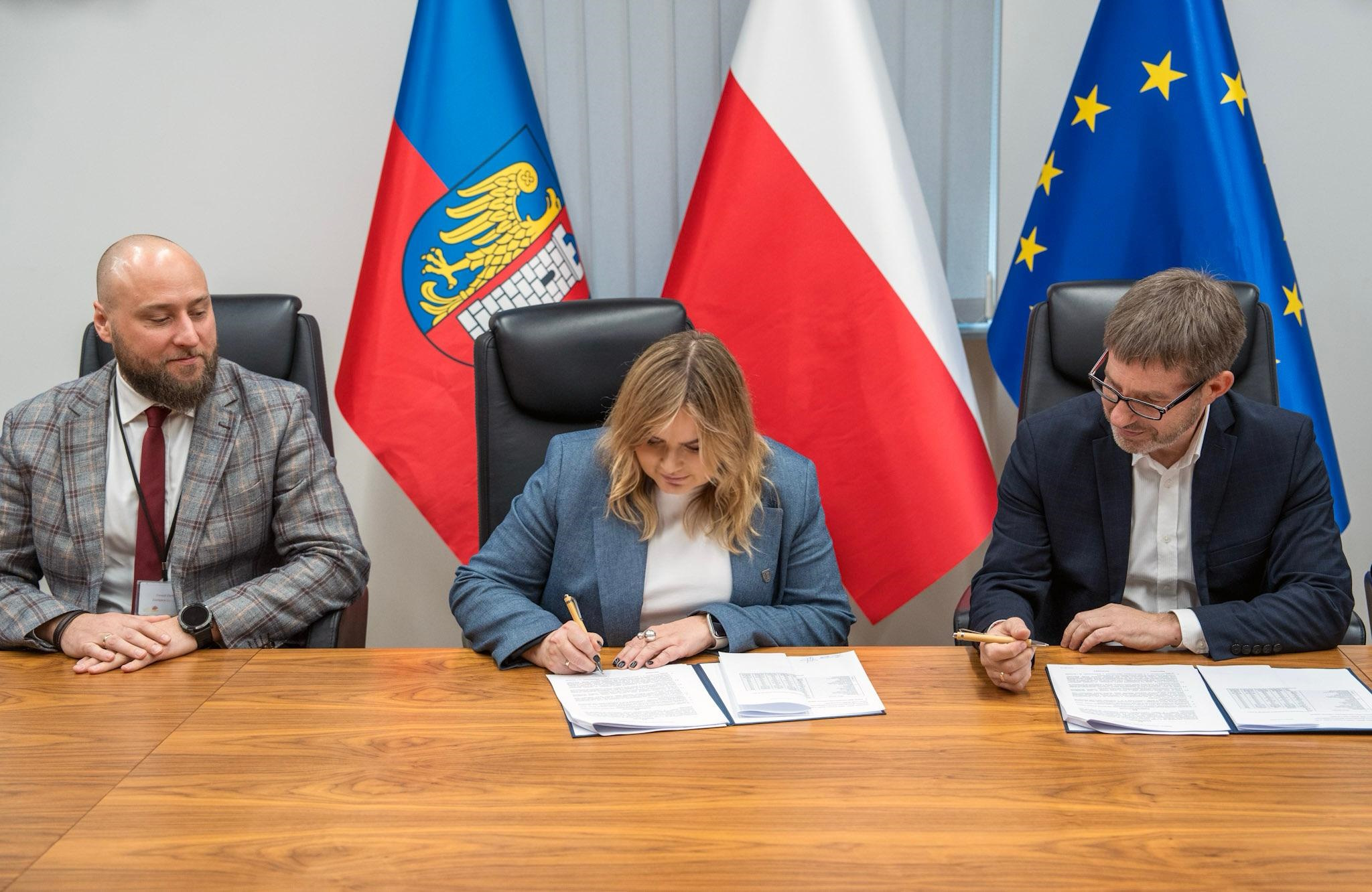 prezydent Gliwic z prezesem zarządu i dyrektorem Mostostalu oraz dyrektorem ZDM podpisują umowę. Siedzą za stołem, za nimi są flagi