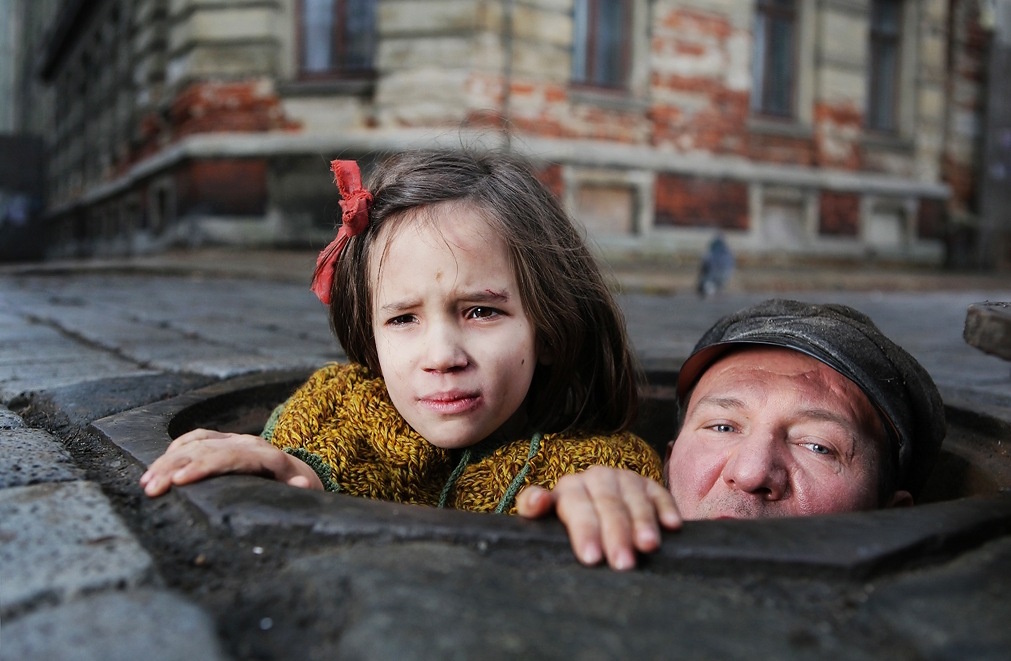 Mężczyzna i dziewczynka wychodzą ze studzienki kanalizacyjnej (kadr z filmu „W ciemności”)