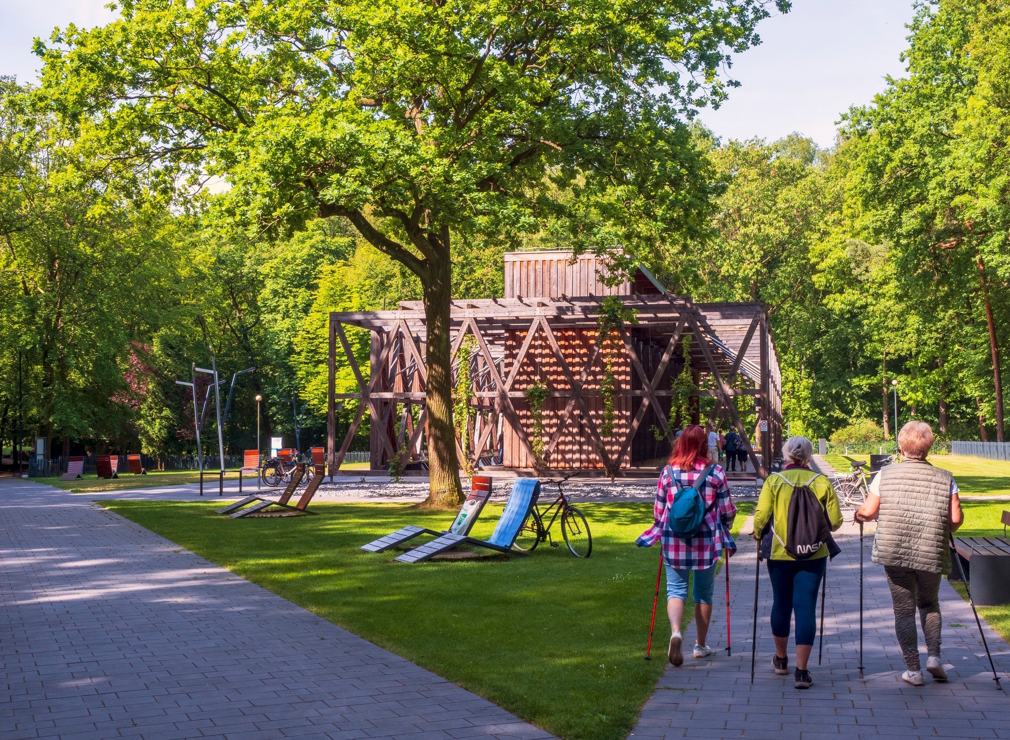 trzy kobiety z kijkami spacerują przy tężni, wokół dużo zieleni