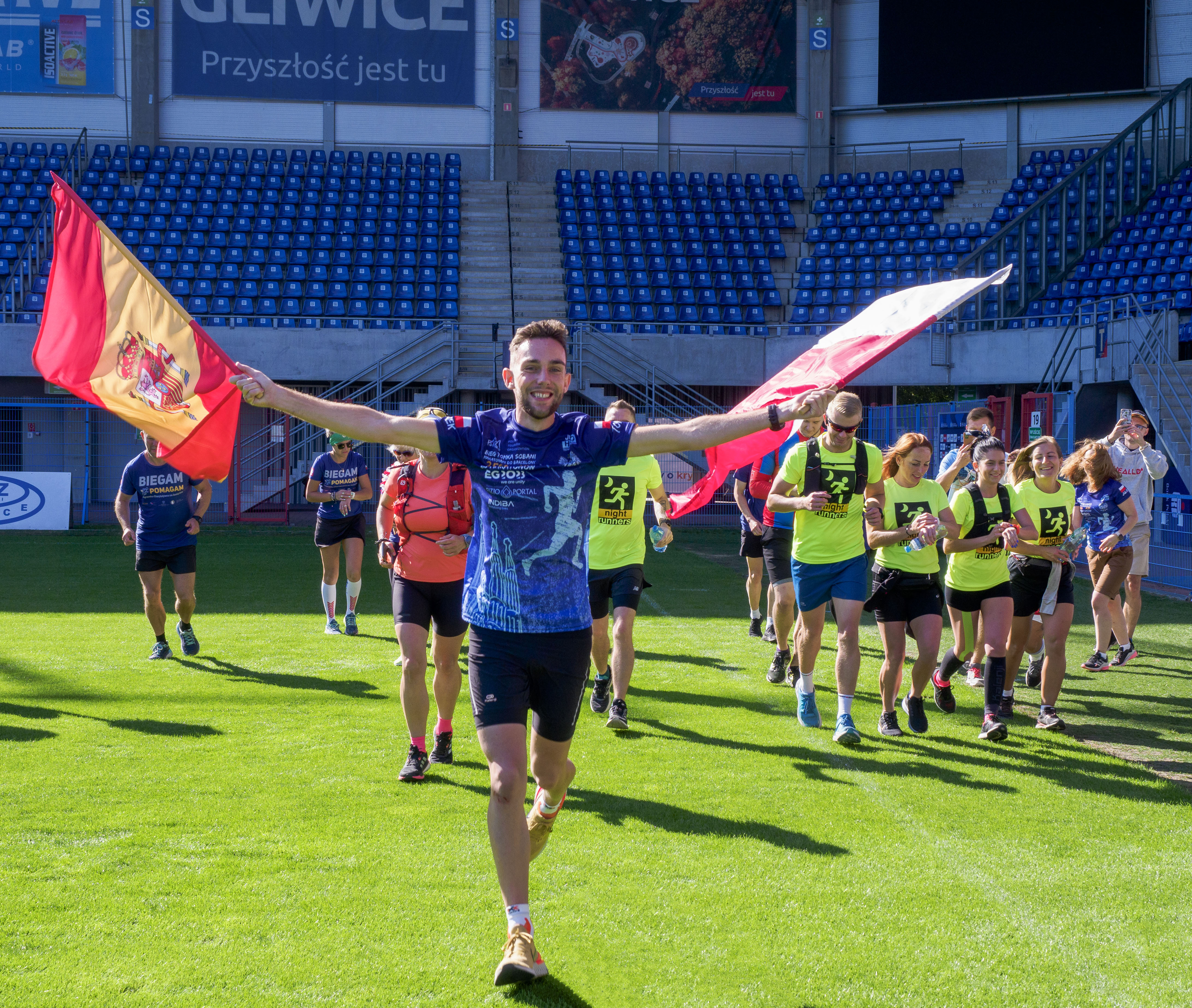 Tomasz Sobania z flagami Polski i Hiszpanii na murawie stadionu