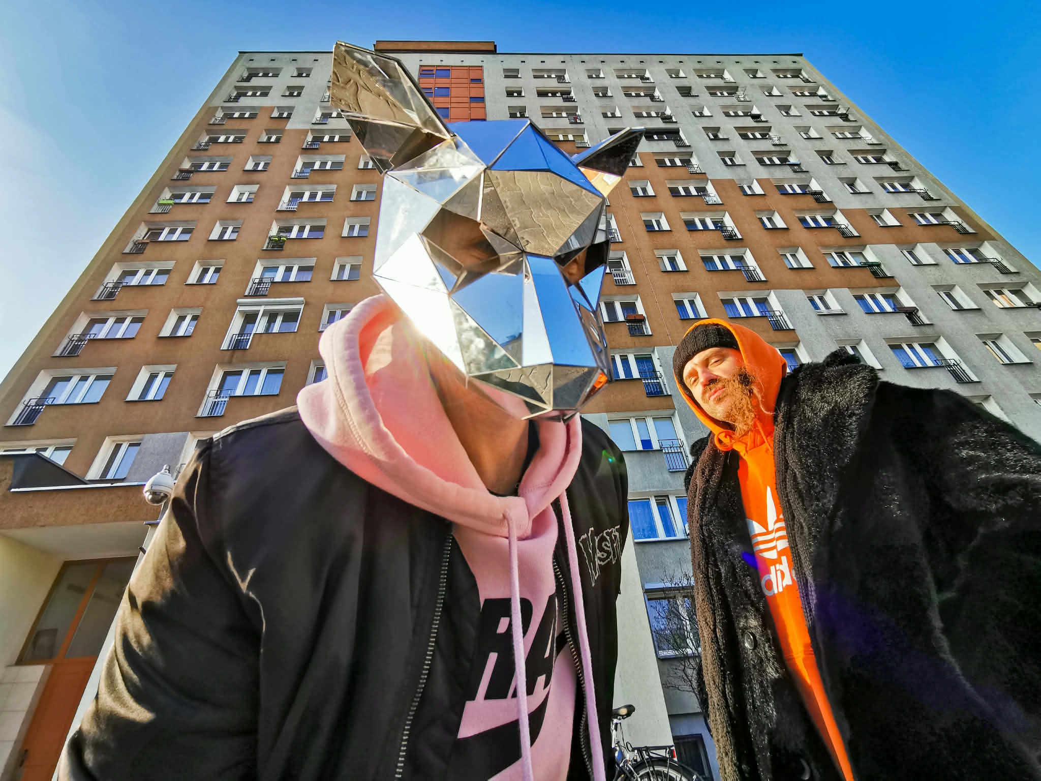 Dwóch mężczyzn, jeden w masce, w tle wieżowiec