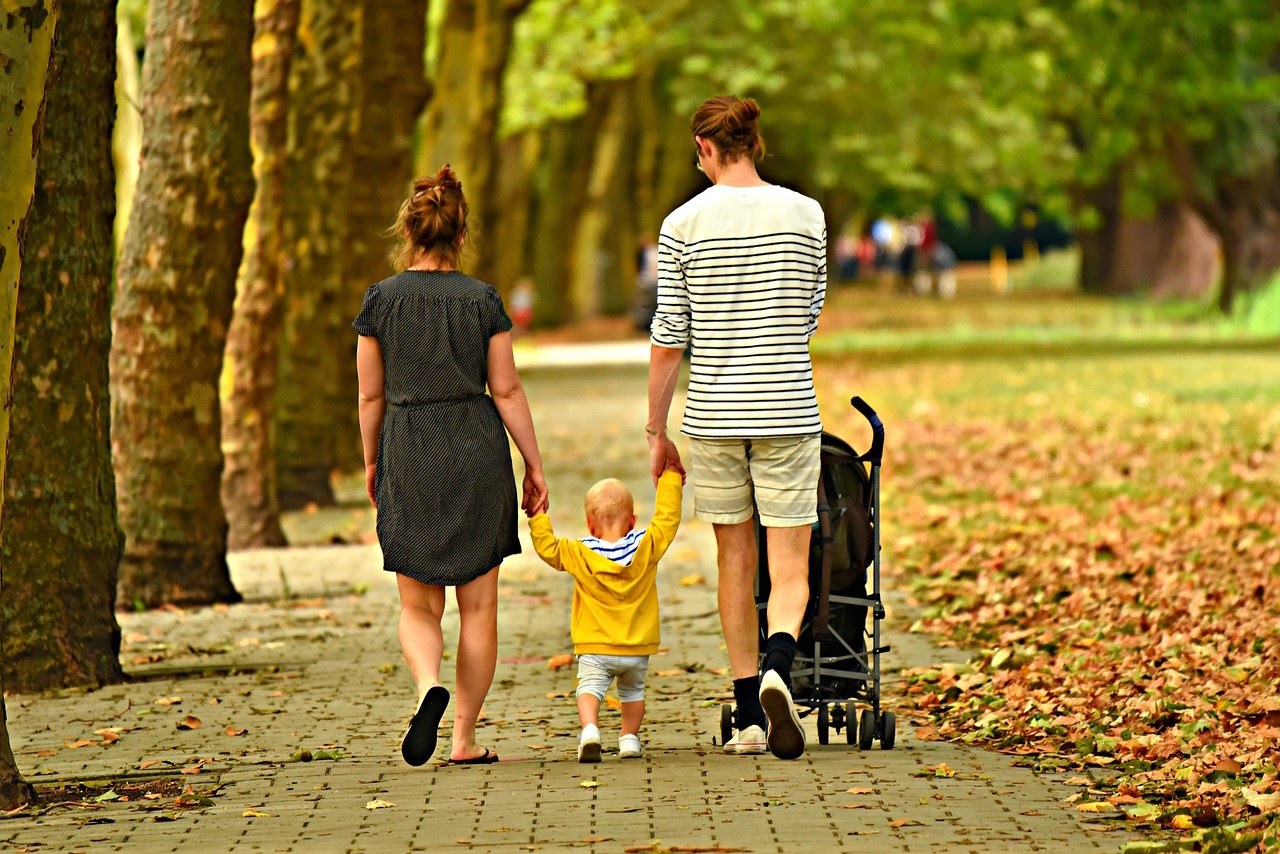 rodzice i dziecko z wózkiem idą przez jesienny park