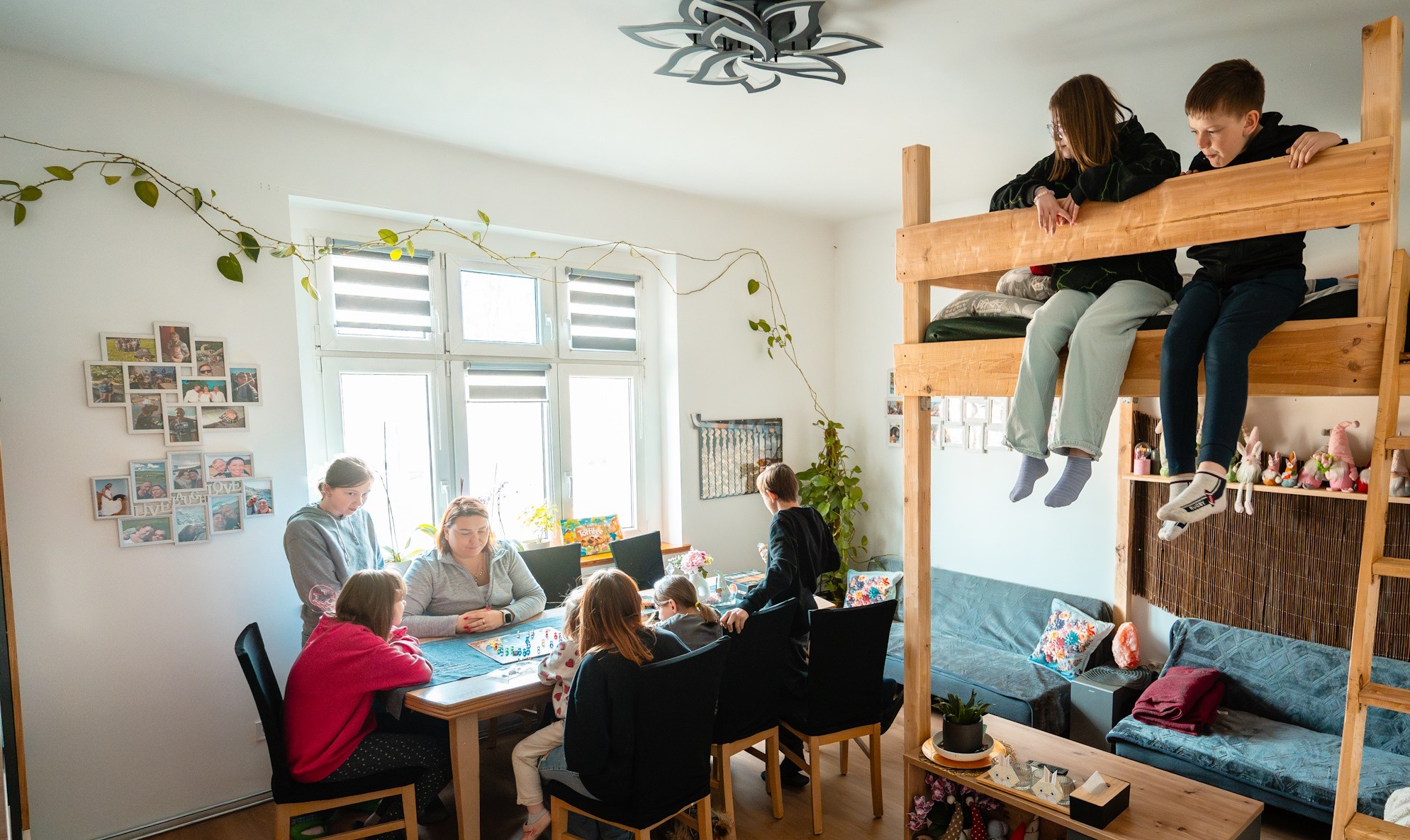 kobieta z dziećmi przy stole gra w planszówki, dwoje dzieci siedzi na piętrowym łóżku