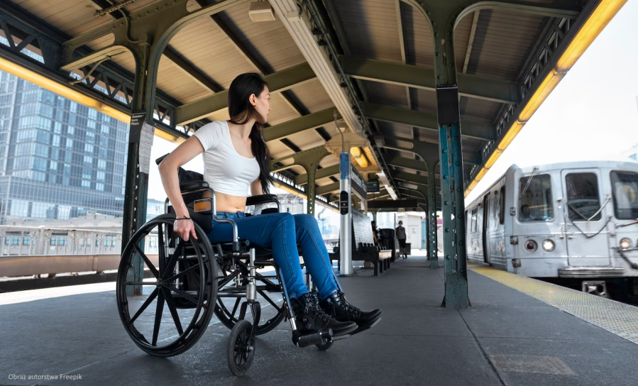 Młoda kobieta na wózku inwalidzkim oczekuje na dworcu kolejowym na wjeżdżający pociąg.